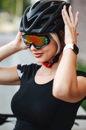 Photo for Fitness young woman in protective helmet and sport glasses posing on city street. Caucasian lady with smart watch on wrist preparing for morning cycling on fresh air. - Royalty Free Image