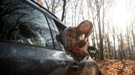 Photo for Long-haired brunette on the auto background. Female model is wearing warm clothes. Autumn concept. Autumn forest journey by car - Royalty Free Image