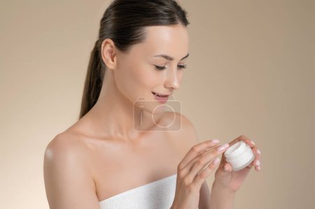 Photo for Charming caucasian woman with healthy fresh skin applying cream on face. Isolated over beige background. Female model taking care of natural beauty. - Royalty Free Image