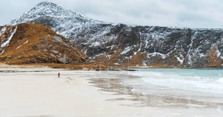 Foto de Mujer caminando a lo largo de una playa marina vacía Kvalvika y mirando a las montañas. Fiordo en Noruega. Vista panorámica. Viaje, aventura. Sentido de libertad, estilo de vida. Islas Lofoten, Noruega. Norte de invierno - Imagen libre de derechos