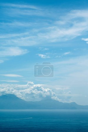 Foto de Paisaje de mar azul y montañas en las nubes en un soleado día de verano. Pequeño barco navegando a la isla griega - Imagen libre de derechos