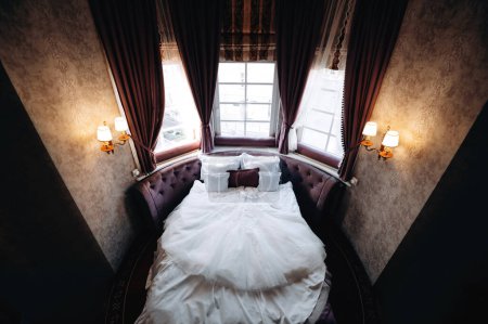 Foto de Increíblemente hermoso vestido de novia acostado en la cama en el interior de la habitación de hotel clásico con grandes maravillas panorámicas - Imagen libre de derechos