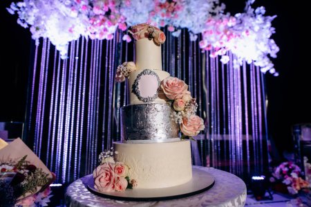 Téléchargez les photos : Rayon bas angle d'élégance Gâteau de mariage décoré de fleurs et de rubans sur la table. Décoration du soir et lumières colorées - en image libre de droit