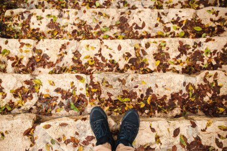 Photo for Feet in black sneakers shoes on the steps of the stairs with autumn leaves - Royalty Free Image