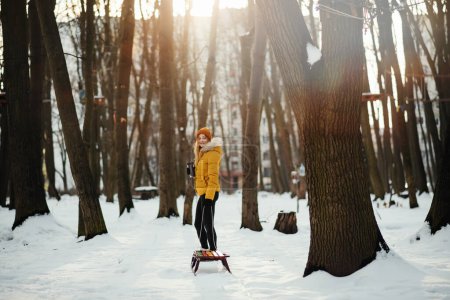 Téléchargez les photos : Belle jeune femme en veste d'hiver jaune avec traîneau marchant dans la forêt d'hiver. - en image libre de droit