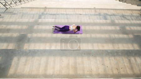 Photo for Top view of sportswoman do abs on fitness mat on concrete platform. Back view of beautiful girl doing exercise in sportswear and sneakers. Concept of sport at outdoors. Sunny daytime - Royalty Free Image
