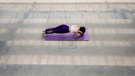 Photo for Top view of sportswoman do abs on fitness mat on concrete platform. Back view of beautiful girl doing exercise in sportswear and sneakers. Concept of sport at outdoors. Sunny daytime - Royalty Free Image