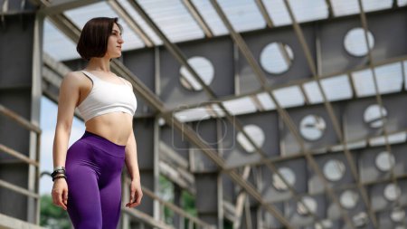 Photo for European sportswoman stand and enjoy view on fitness mat on concrete stairs of stadium. Young beautiful girl with short hair wear sportswear and sneakers. Concept of sport at outdoors. Sunny day - Royalty Free Image
