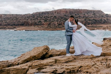 Téléchargez les photos : Photo romantique de jeunes mariés amoureux embrassant sur le fond du paysage de la mer et des rochers de Chypre. Séance photo de mariage, lune de miel des jeunes mariés
. - en image libre de droit