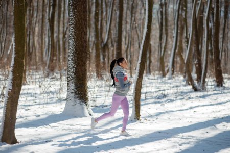 Photo for Fast slim sportswoman running in forest at snowy winter day. Race, jogging in nature, winter fitness - Royalty Free Image