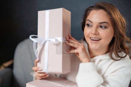 Téléchargez les photos : Portrait de la femme surprise posant avec des boîtes cadeaux alors qu'elle était assise sur le canapé. Noël vacances concept - en image libre de droit