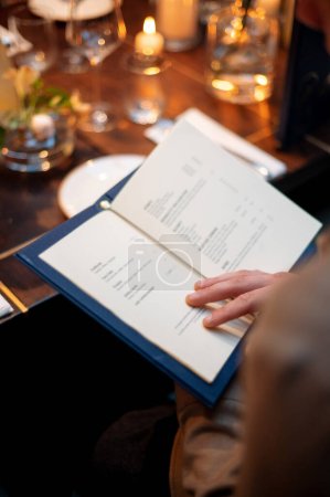 Téléchargez les photos : Femme lisant un menu dans un restaurant. Concentrez-vous sélectivement sur le livre. Bougies avec lumière chaude et dîner sur fond - en image libre de droit
