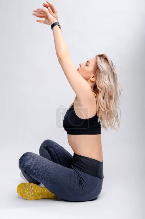 Foto de Mujer rubia joven en ropa deportiva con estilo practicando yoga sobre fondo gris estudio. Ejercicios de estiramiento. - Imagen libre de derechos