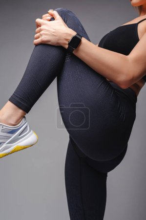 Photo for Cropped view of sporty woman in stylish sportswear stretching legs isolated on grey. Healthy and fitness concept - Royalty Free Image