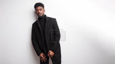 Photo for Serious young bearded guy in black clothes looking to the camera while standing against white background. Human appearance concept - Royalty Free Image