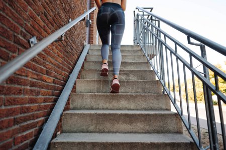 Photo for Close-up of young slim woman running up the stairs outdoors. Sporty girl wearing in stylish tight leggings and sneaker - Royalty Free Image