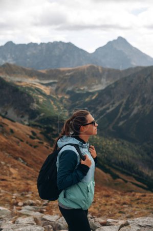 Photo for Stylish young woman with backpack and sunglasses standing on top of a mountain and looking to the Tatra rocks, Slovakia - Royalty Free Image