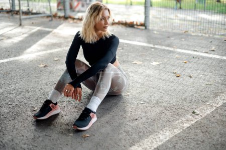 Photo for Hipster blonde girl in fashion sportswear relaxing and posing after fitness exercise in the street. Outdoor sports, urban style and healthy lifestyle concept - Royalty Free Image