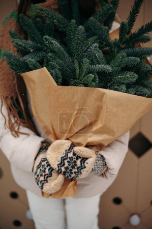 Photo for Close uo view of girl in gloves holds a bouquet of Christmas trees in her hands. Winter snowy day - Royalty Free Image