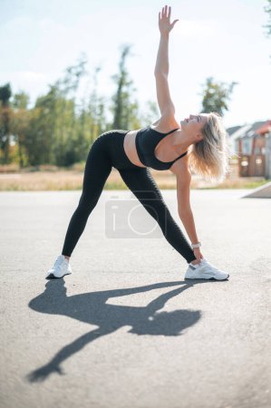 Foto de Largura completa de tiro de la mujer joven en forma haciendo ejercicio de estiramiento solo en la calle. Sexy modelo de fitness haciendo ejercicio en la mañana al aire libre - Imagen libre de derechos