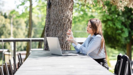 Photo for European dissatisfied businesswoman work on laptop computer outdoors. Beautiful young girl sit at table in sunny park. Modern woman lifestyle. Concept of remote and freelance work - Royalty Free Image
