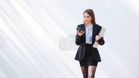 Photo for European businesswoman use cellphone. Focused pretty young girl wear formal suit and stand on white background. Modern woman lifestyle. Concept of remote and freelance work. Copy space - Royalty Free Image