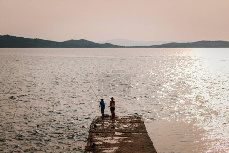 Téléchargez les photos : Deux pêcheurs pêchent dans la mer lors d'un magnifique coucher de soleil à Ouranoupolis, Grèce - en image libre de droit