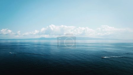 Foto de Dos barcos nadando en el increíble paisaje azul del mar y el cielo en Grecia. Silueta de las montañas al fondo - Imagen libre de derechos