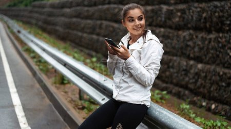 Téléchargez les photos : Touriste souriante utilisant un téléphone portable moderne à l'extérieur. Heureuse femme caucasienne randonnée avec sac à dos parmi les montagnes. Concept de personnes et de technologie. - en image libre de droit