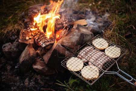 Téléchargez les photos : Grilling sausages. Concept of resting in the fresh air, frying sausages on the grill. Sausages, bread, vegetables barbecue - en image libre de droit
