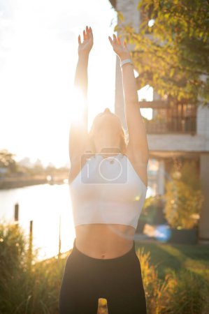 Foto de Señora caucásica enfocada estirando las manos mientras está parada en la esterilla de yoga afuera, disfrutando del verano. Concepto de estilo de vida deportivo - Imagen libre de derechos