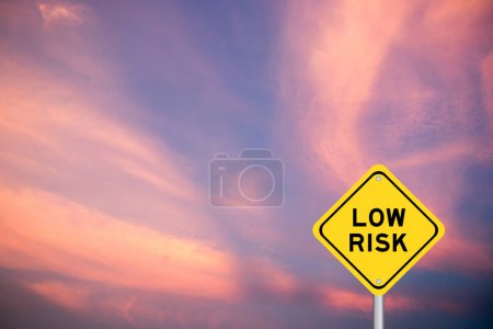 Signo de transporte amarillo con palabra de bajo riesgo sobre fondo de cielo de color violeta