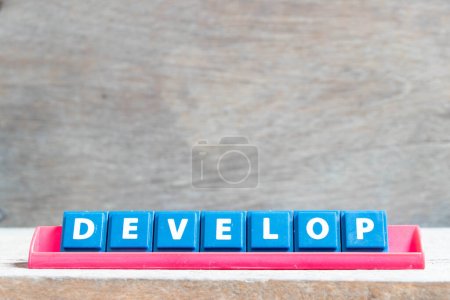 Foto de Letra del alfabeto del azulejo con la palabra desarrollar en estante de color rojo sobre fondo de madera - Imagen libre de derechos