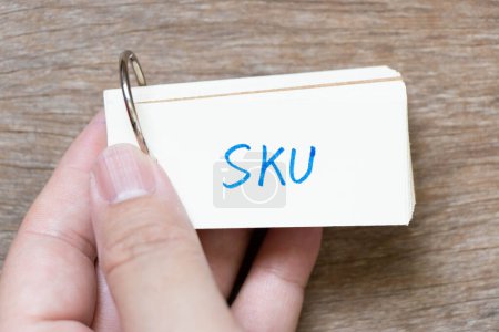 Téléchargez les photos : Main tenir la carte flash avec écriture manuscrite dans le mot SKU (Abréviation de l'unité de stockage) sur fond de bois - en image libre de droit