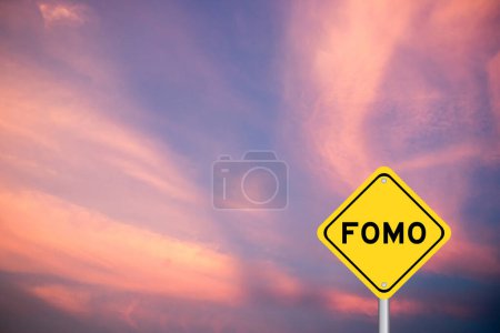 Signo de transporte amarillo con palabra FOMO (abreviatura de miedo a perderse) sobre fondo de cielo de color violeta