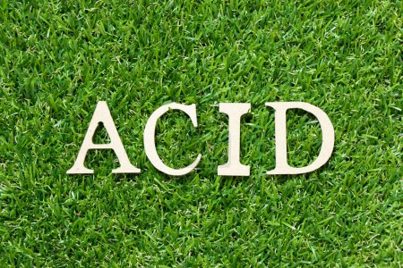 Téléchargez les photos : Lettre en bois dans le mot acide sur fond d'herbe verte - en image libre de droit