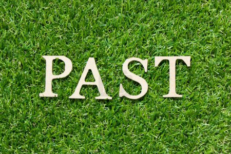 Téléchargez les photos : Lettre en bois dans le mot passé sur fond d'herbe verte - en image libre de droit