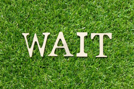 Wood letter in word wait on green grass background