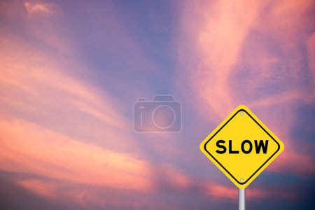 Foto de Signo de transporte amarillo con palabra lenta sobre fondo de cielo de color violeta - Imagen libre de derechos