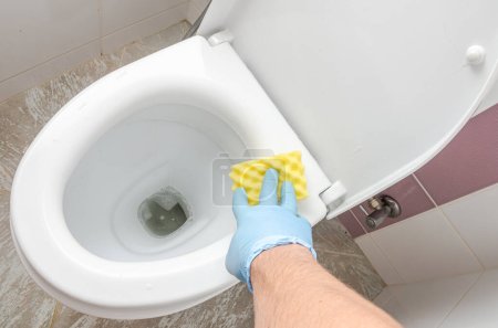 Foto de Una ama de llaves lava un inodoro sucio con un agente de limpieza en el inodoro - Imagen libre de derechos