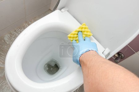 Téléchargez les photos : Une femme de ménage lave un bol de toilette sale avec un agent de nettoyage dans les toilettes - en image libre de droit