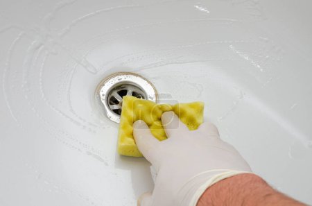 Téléchargez les photos : Femme de ménage lavant une baignoire avec des produits chimiques ménagers dans la salle de bain - en image libre de droit