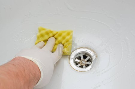 Téléchargez les photos : Femme de ménage lavant une baignoire avec des produits chimiques ménagers dans la salle de bain - en image libre de droit