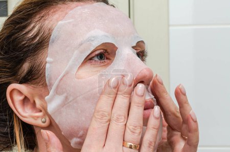 Téléchargez les photos : Jeune femme faisant masque de feuille sur son visage pendant les traitements de spa de beauté - en image libre de droit