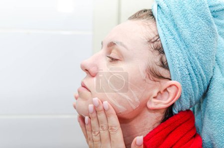 Téléchargez les photos : Jeune femme faisant elle-même un soin de beauté spa en déposant un masque de drap hydratant dans la salle de bain, après une douche - en image libre de droit