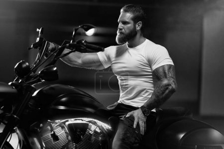 Foto de Sexy guapo atractivo deportivo modelo de fitness musculoso motero empanado en camiseta blanca apretada se sienta en la hermosa motocicleta brutal en el aparcamiento, foto en blanco y negro - Imagen libre de derechos