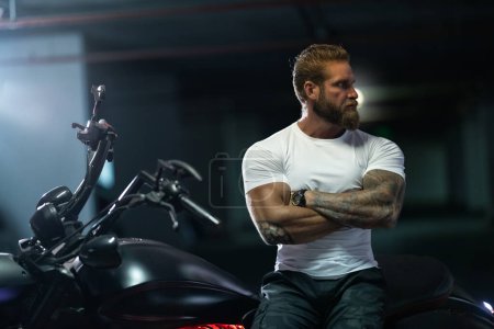 Foto de Sexy guapo atractivo deportivo muscular fitness modelo empanado motorista en blanco apretado camiseta se sienta en brutal hermosa motocicleta en el aparcamiento - Imagen libre de derechos