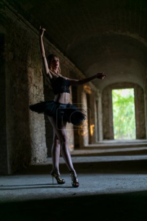 A ballerina gracefully performs in a dark room wearing a black tutu, showcasing her balance and artistry in the realm of performance art