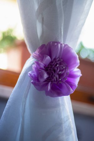 Ein weißer Vorhang, der mit einer lila Blume geschmückt ist, verleiht dem Dekor einen Hauch von Farbe. Die künstliche Magenta-Blume bringt einen lebendigen Pop in den Raum