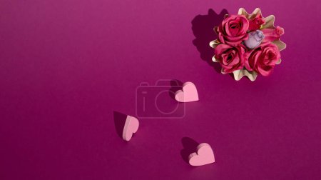 Téléchargez les photos : Roses dans une boîte à muffins avec petits cœurs sur un fond violet concept créatif minimal - en image libre de droit
